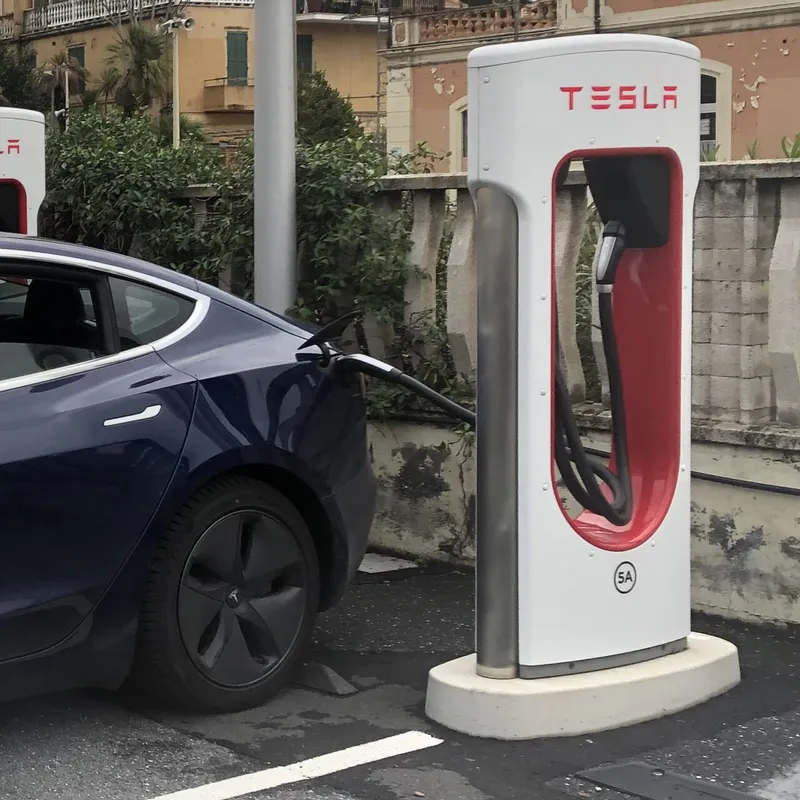 Un Tesla Model 3 cargando en un Supercargador de doble cable — el modelo cuyo lugar de fabricación está en el centro del conflicto